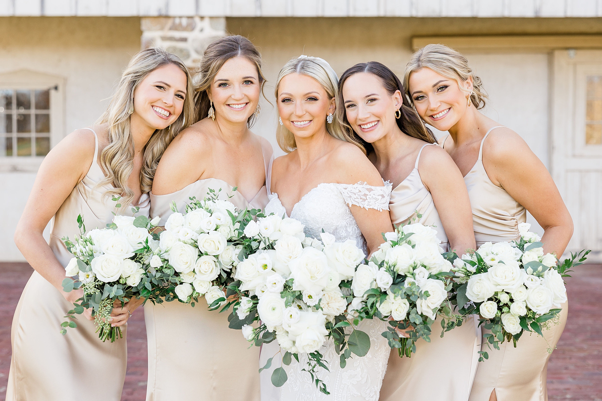 bride and bridesmaids in champagne dresses holding white wedding bouquets 