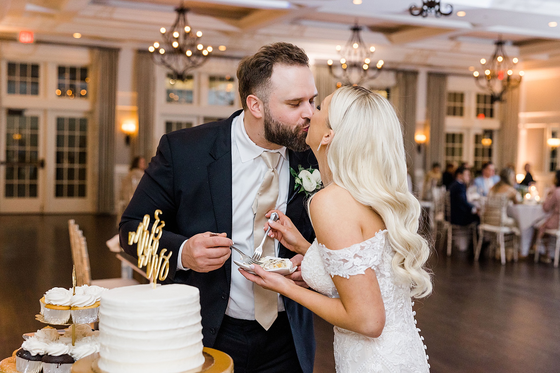 bride and groom kiss as they eat cake at wedding reception