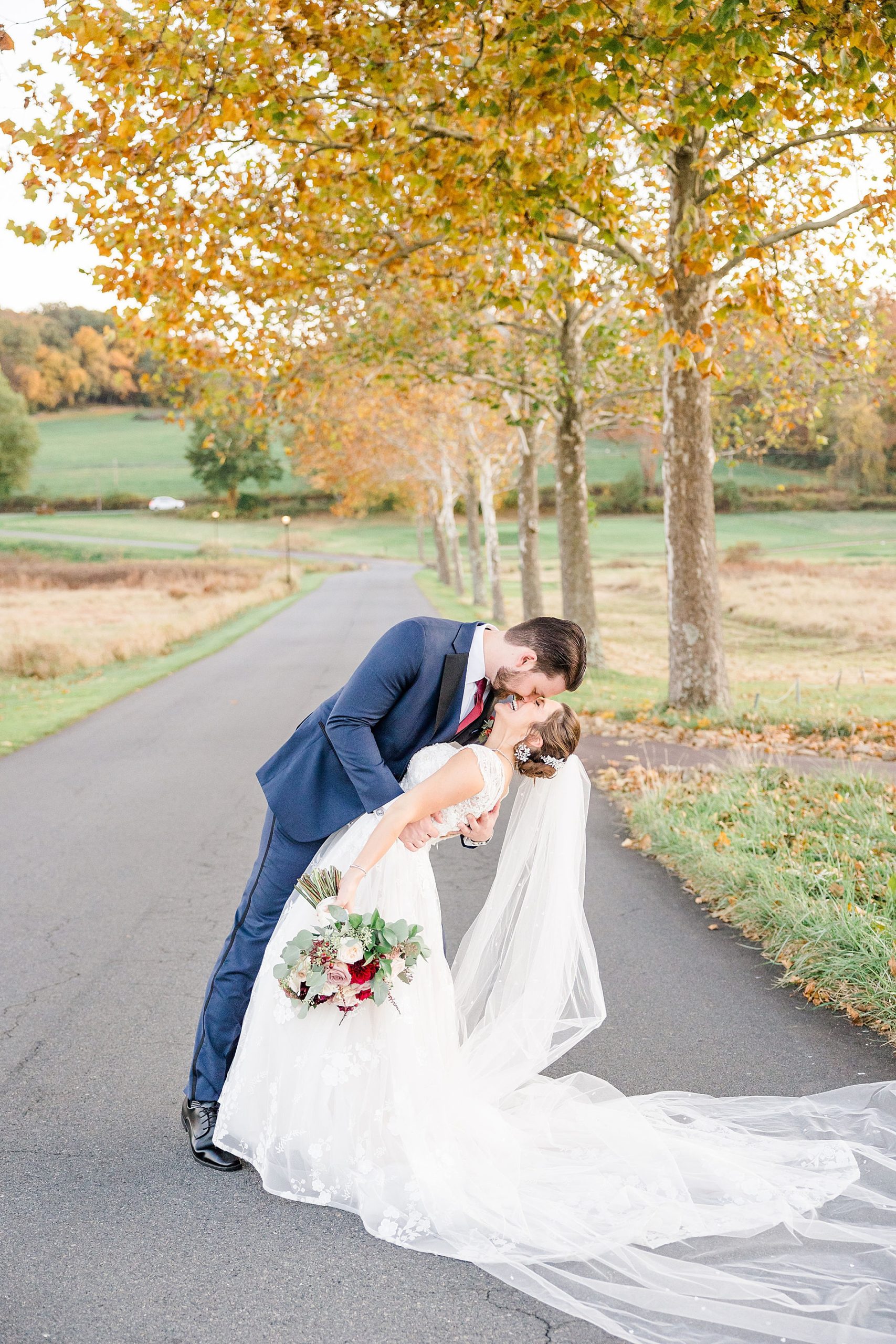 bride and groom kiss in road during fall wedding portraits