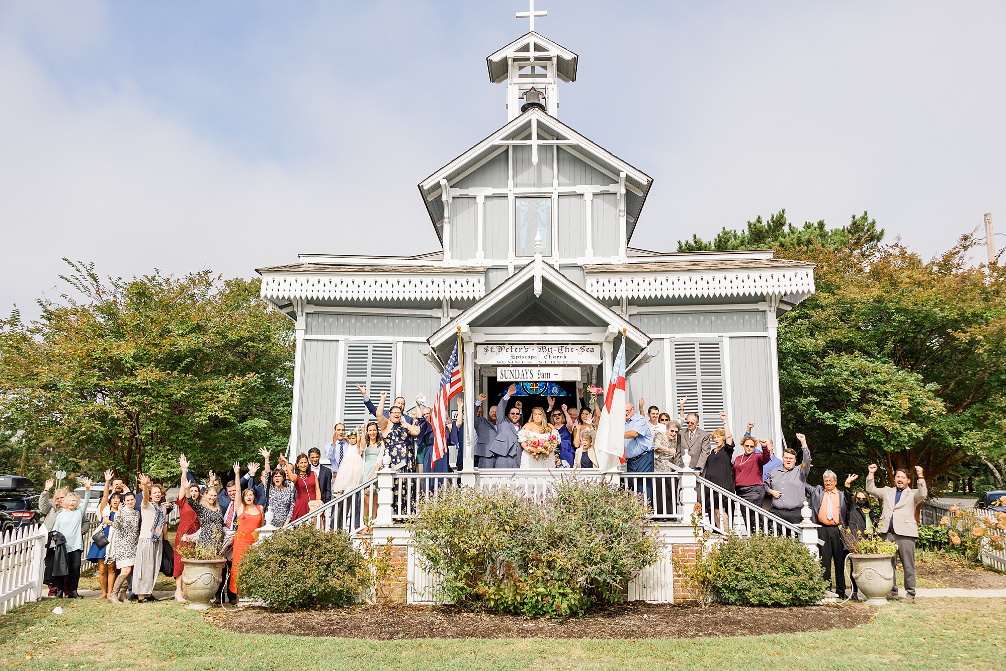 Wedding guests stand with bride and groom in front of church 