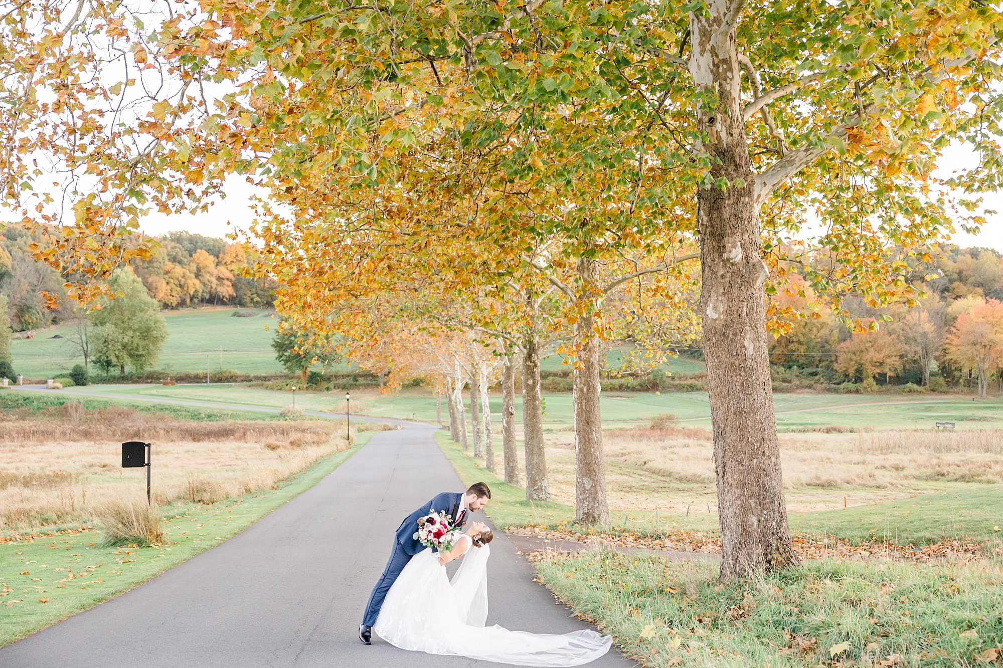groom dips fiance under fall trees during wedding portraits