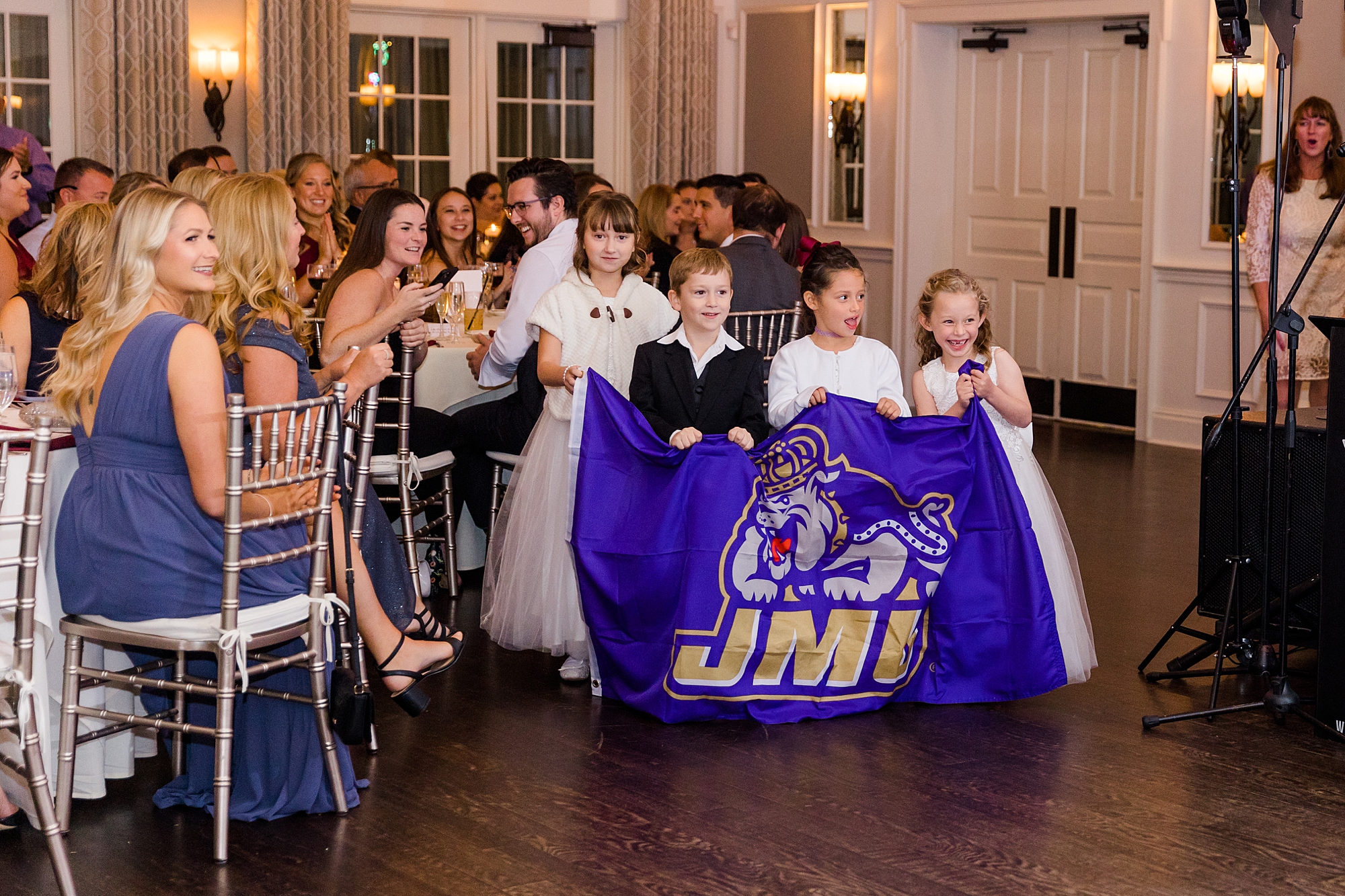 flower girls and ring bearers enter wedding reception holding JMU banner