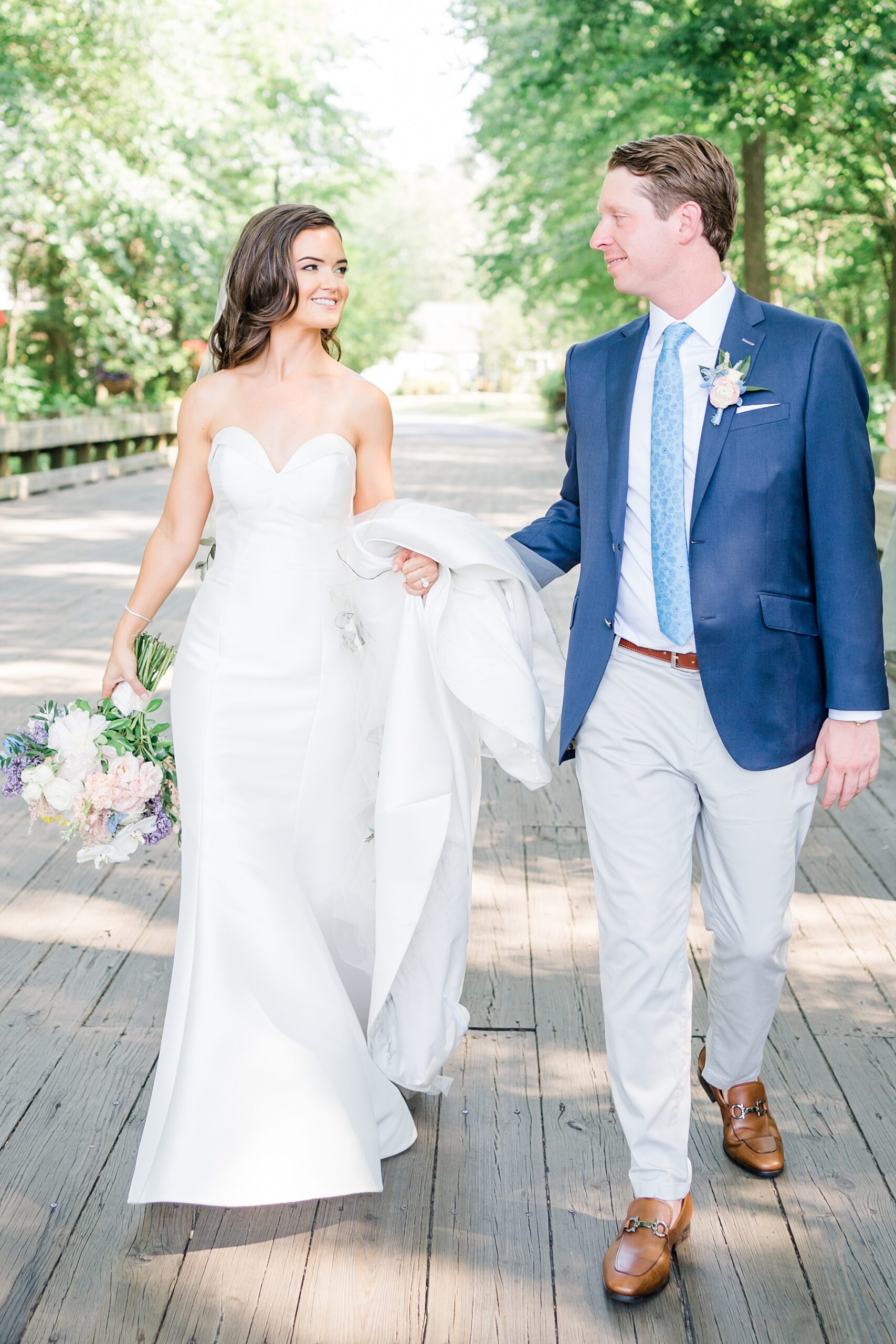 bride and groom walk together down wooden bridge 