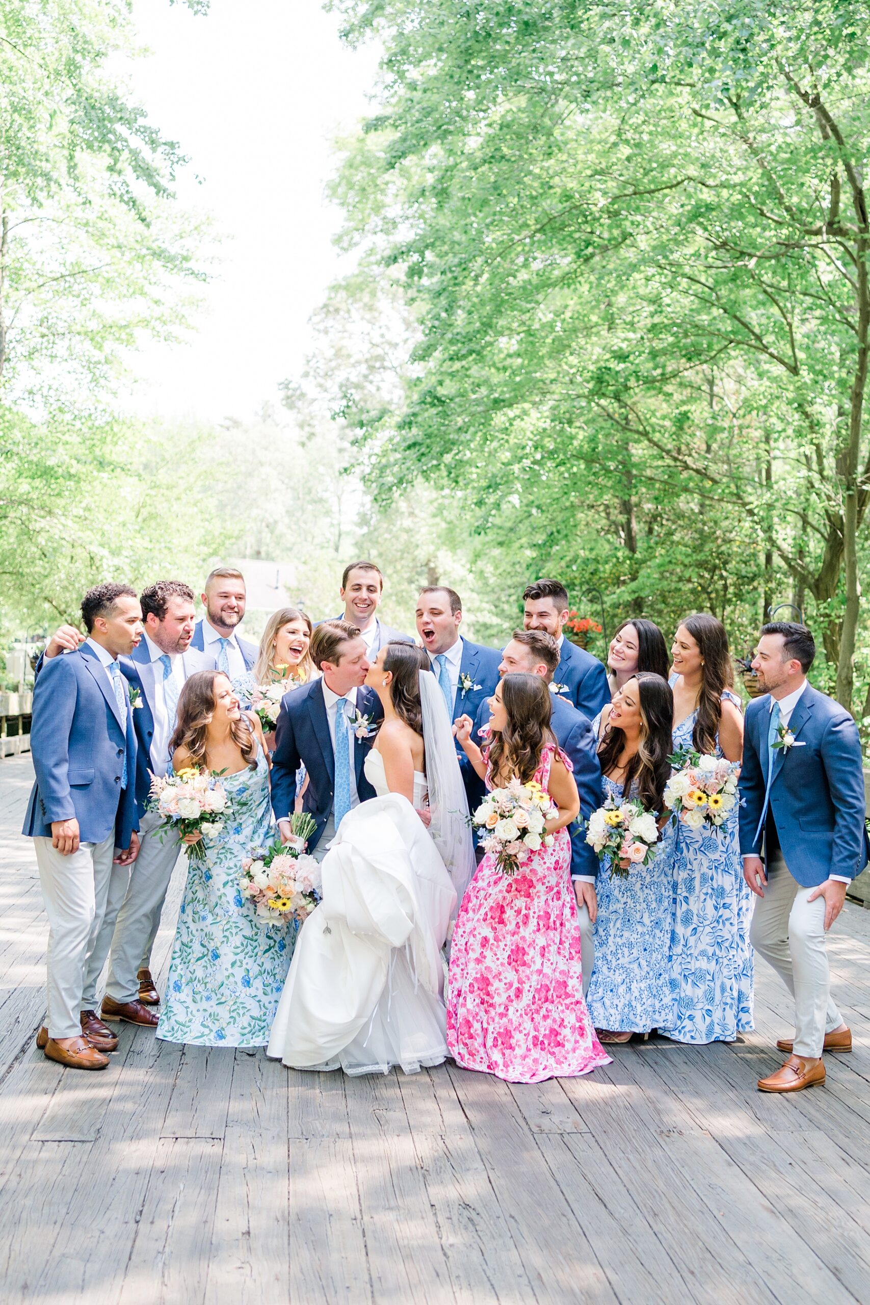 bridal party stand around bride and groom as they kiss