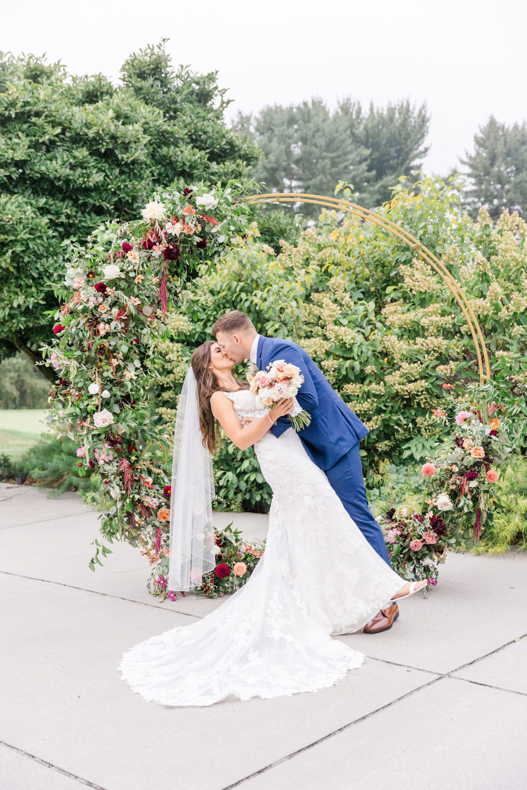 bride and groom kiss in front floral decorated circular wedding arch