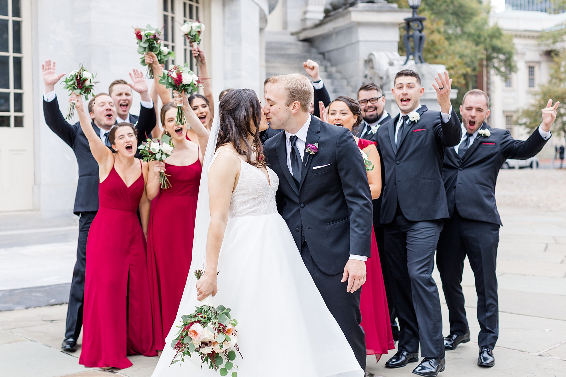 bridesmaids and groomsmen cheer as bride and groom kiss