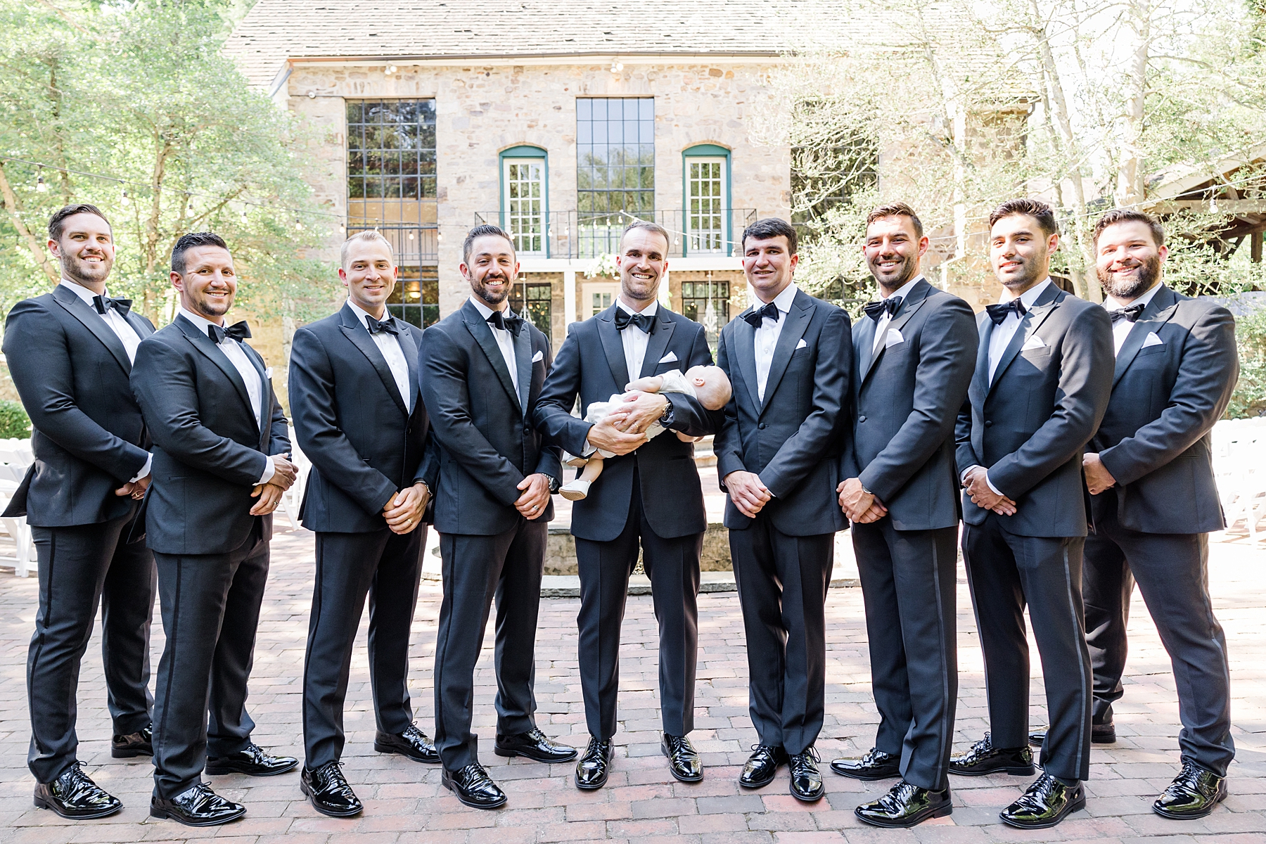 groom holding baby son with groomsmen