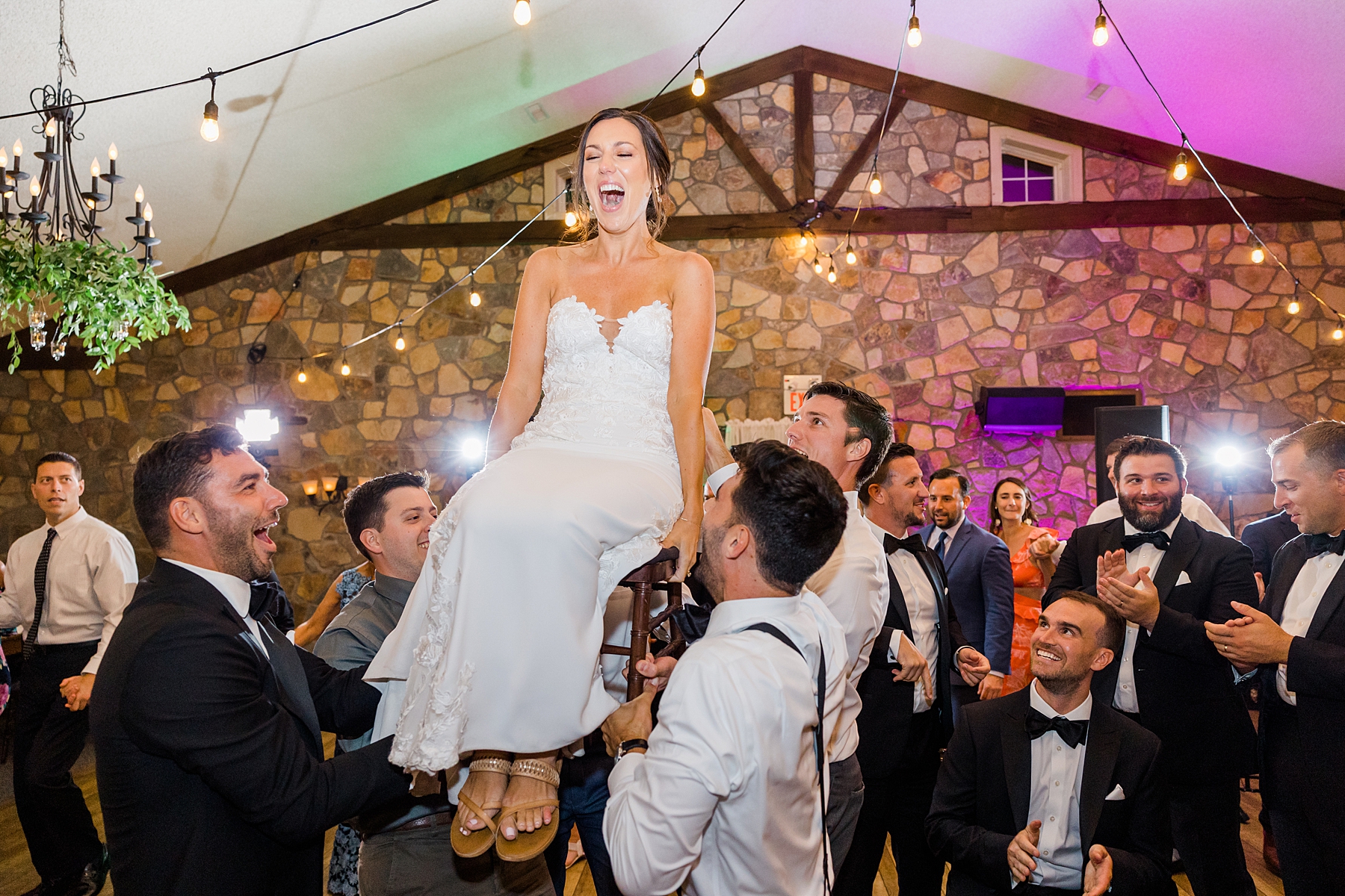 bride is lifted up on chair by groomsmen at reception 